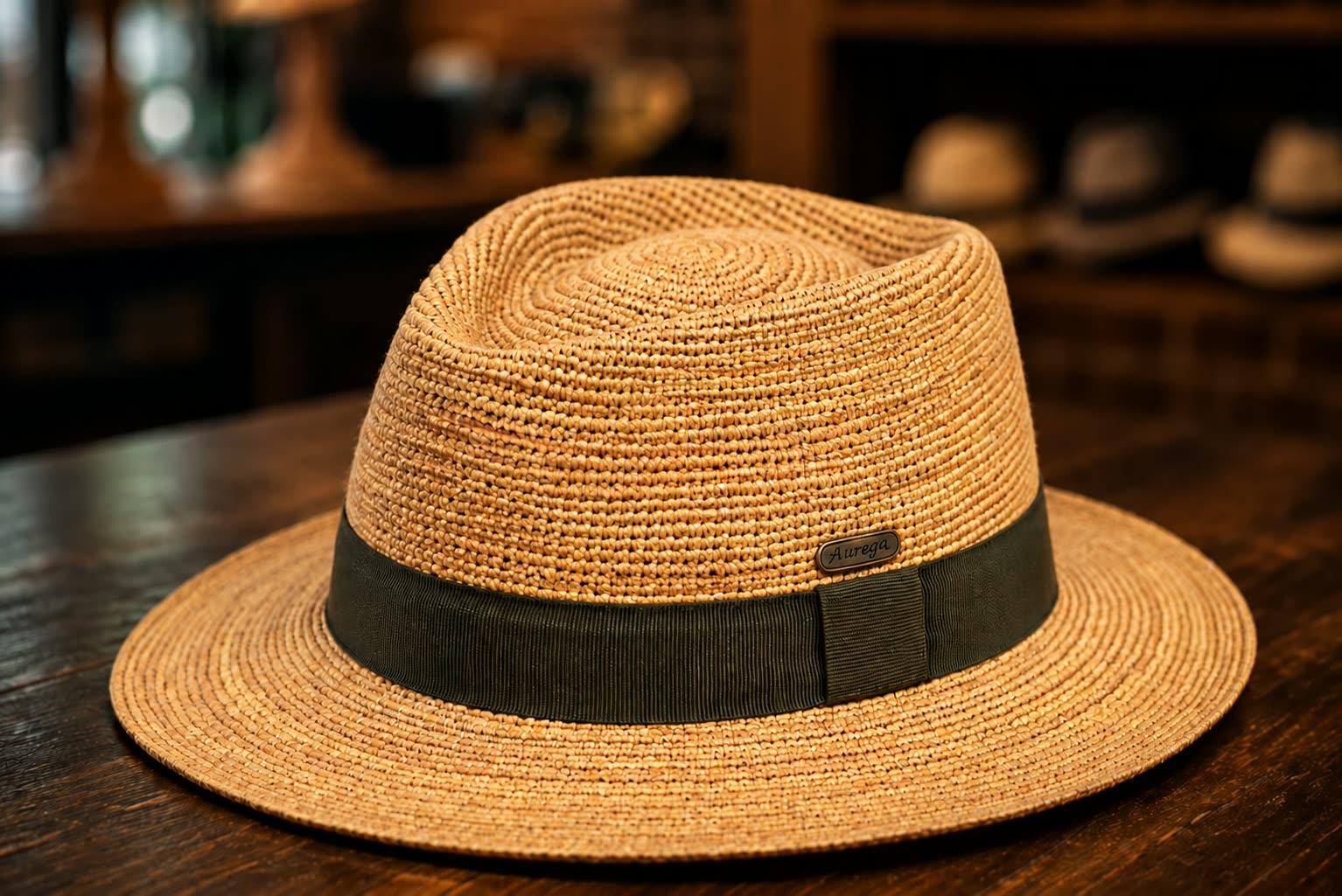 Fedora en raphia crocheté au ruban kaki, posé sur une table en bois de la boutique