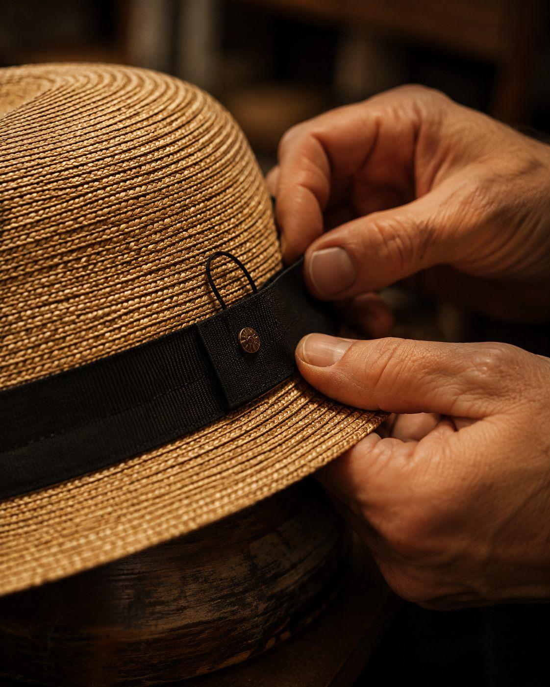 Deux mains ajustent le gros-grain noir et son insigne sur un chapeau de paille